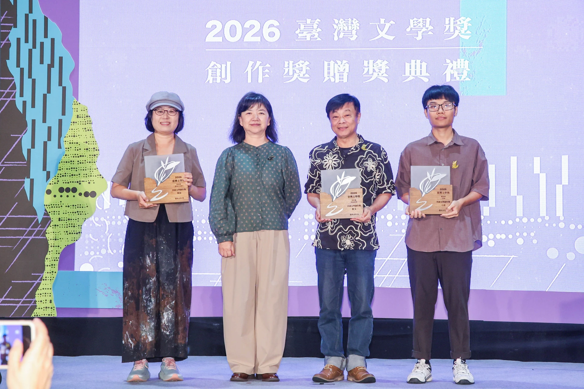 文化部政務次長李靜慧與台語文學創作獎三位得獎者黃鈺婷、張政愉、陳柏鈞在背板前合影。